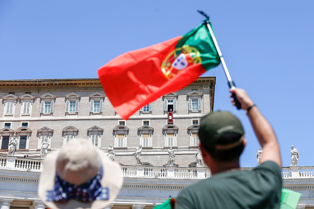 A man waves a Portuguese flag as Pope Francis prays the Angelus with visitors gathered in St. Peter's Square at the Vatican July 9, 2023. (CNS photo/Lola Gomez)