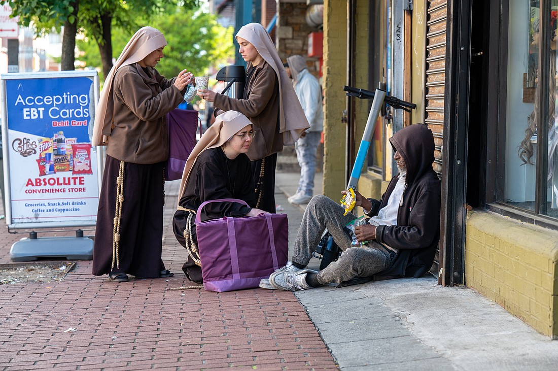Sister Giovana of the Most Holy Name of Jesus (squatting) joins Sister Samaritan of Scourged Love (left) and Sister Maria Clara of the Crucified in giving food to a man near Lexington Market in Baltimore May 3, 2023. (OSV News Photo/Kevin J. Parks, Catholic Review)