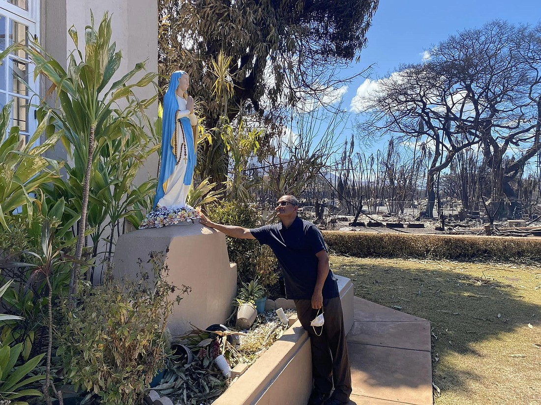 Missionaries of Faith Father Kuriakose Nadooparambil, pastor of Maria Lanakila Church in Lahaina, Maui, Aug. 16, 2023 touches a statue of the Blessed Virgin Mary which still stands amid foliage untouched by the wildfire that scorched trees across the street and destroyed the entire town of Lahaina. (OSV News photo/courtesy Maria Lanakila Parish)