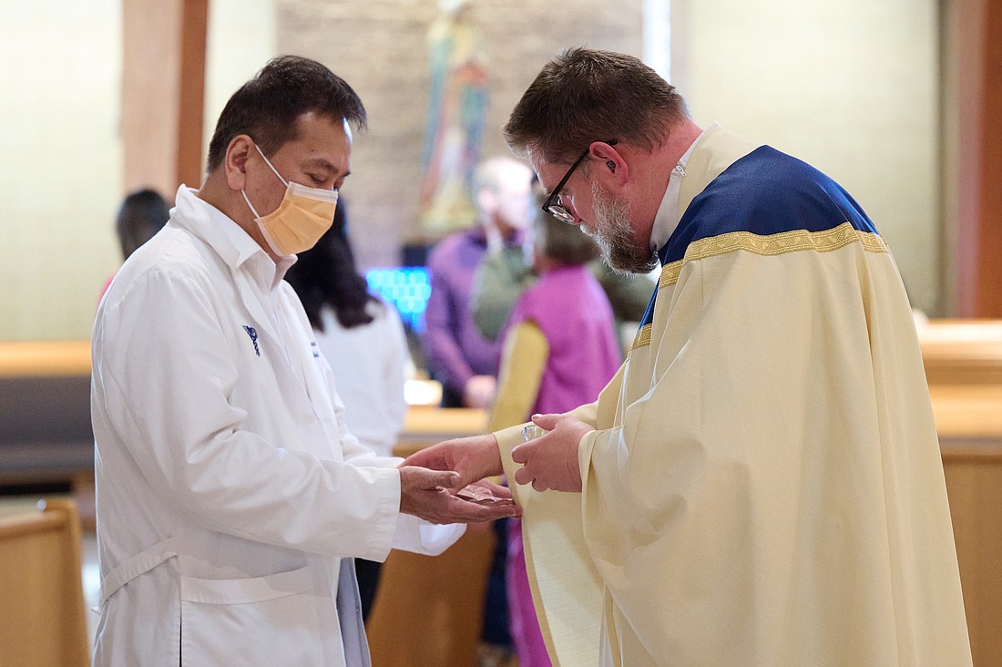 Father Michael Kennedy, administrator of St. Luke Parish, Toms River, blesses a healthcare worker's hands during the White Mass celebrated Oct. 15 in St. Luke Church. Father John Butler celebrated the Mass and Father Kennedy was homilist. Mike Ehrmann photo