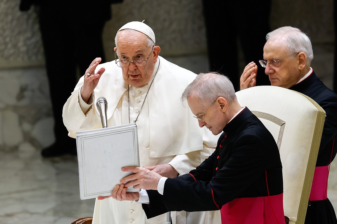 Pope Francis gives his blessing at the end of his weekly general audience as Msgr. Luis Maria Rodrigo Ewart, an aide, holds the pope's prayer book in the Paul VI Audience Hall at the Vatican Dec. 20, 2023. (CNS photo/Lola Gomez)