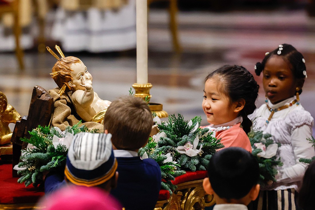 Children place flowers around a figurine of the baby Jesus in front of the main altar of St. Peter’s Basilica during Christmas Mass with Pope Francis at the Vatican Dec. 24, 2023. (CNS photo/Lola Gomez)