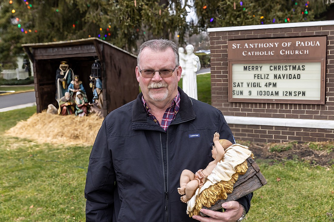 On Christmas Eve, Phil Murray prepares to place the image of the Christ Child in the stable of the outdoor Nativity on the grounds of St. Anthony of Padua Church, Hightstown. Hal Brown photo