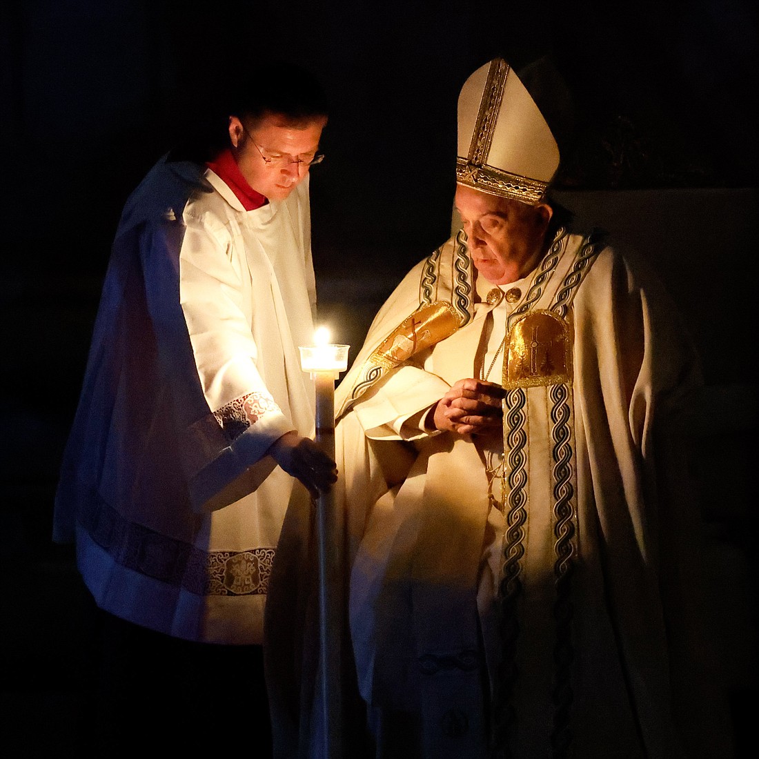 An aide hands Pope Francis his candle, lighted from the paschal candle, at the beginning of the Easter Vigil Mass in St. Peter's Basilica at the Vatican March 30, 2024. (CNS photo/Lola Gomez)