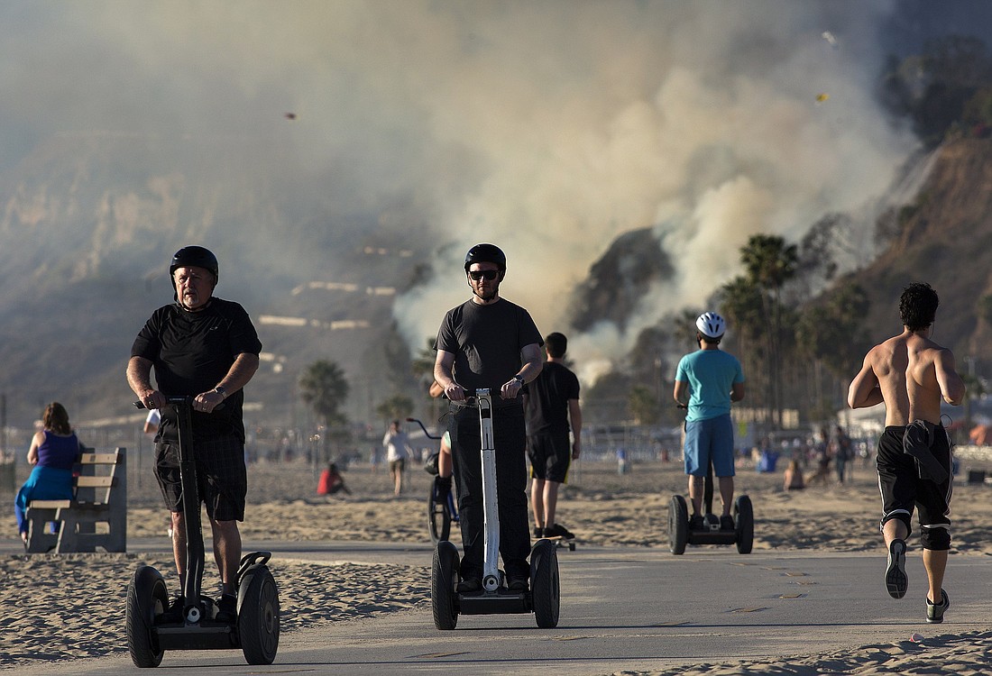 People are pictured in a file photo riding Segway scooters on a bike path as a small brush fire burns on a hillside above Pacific Coast Highway in Pacific Palisades, Calif. (OSV News /Jonathan Alcorn, Reuters)
