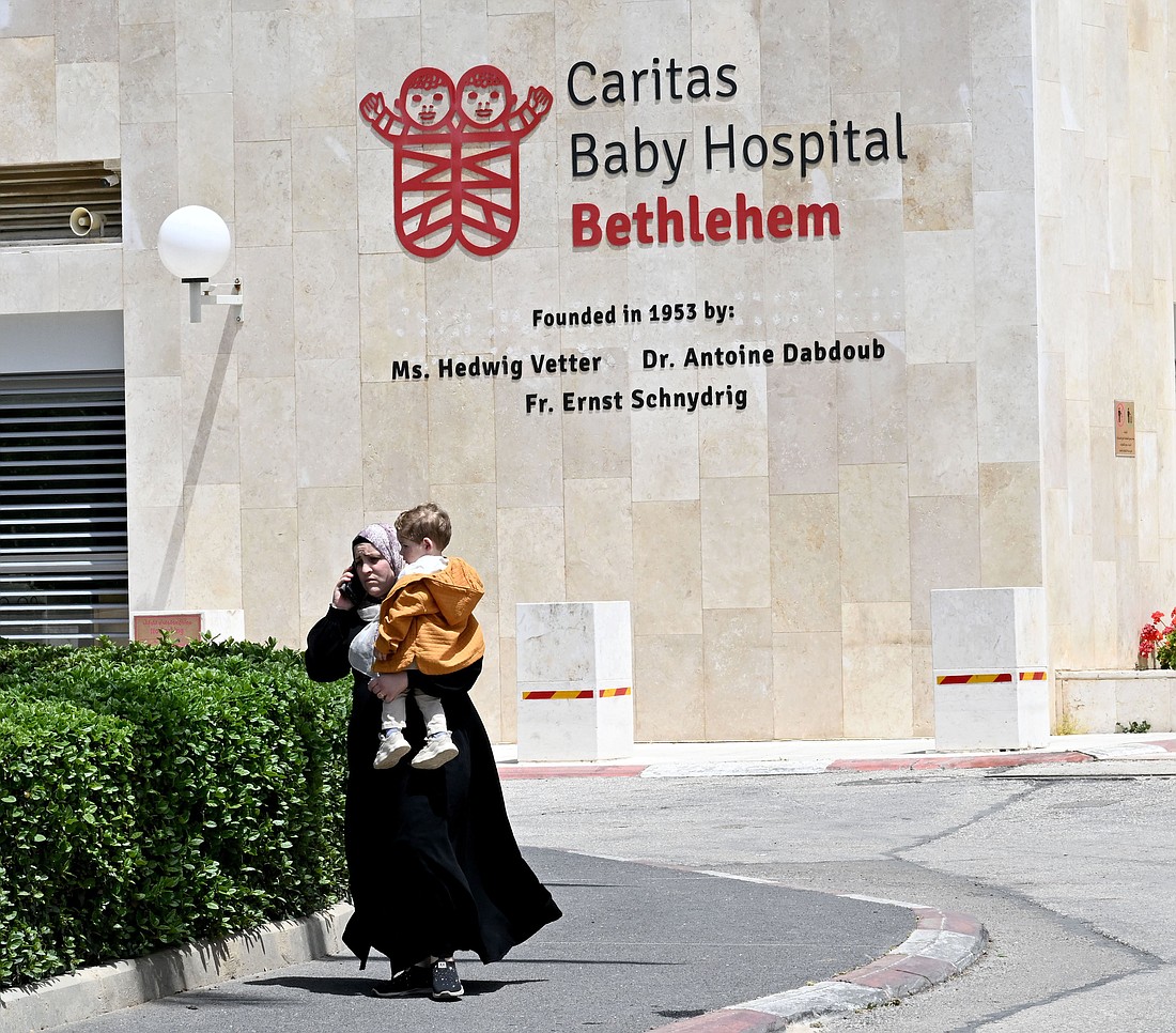 A Palestinian woman talks on the phone while carrying her child outside Caritas Baby Hospital in Bethlehem, West Bank, April 27, 2024. OSV News photo/Debbie Hill