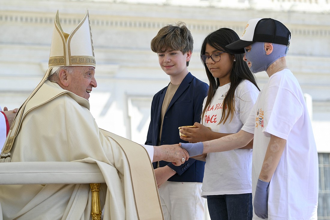 Pope Francis greets children bringing the offertory gifts during Mass in St. Peter's Square at the Vatican May 26, 2024, wrapping up the first World Children's Day held May 25-26. The pope shakes hands with Roman Oleksiv, a Ukrainian boy who lost his mother and suffered life-threatening burns from a Russian missile strike July 14, 2022. (CNS photo/Vatican Media)