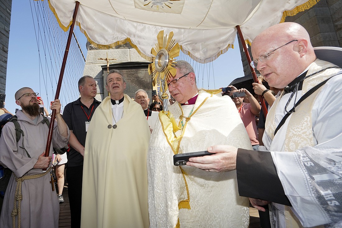 Auxiliary Bishop Gerardo J. Colacicco of  of New York holds the monstrance before transferring it to Bishop Robert J. Brennan, left, of Brooklyn, N.Y., on the Brooklyn Bridge during a Eucharistic procession to Brooklyn from Manhattan on the National Eucharistic Pilgrimage's Seton (East) Route May 26, 2024. On the right is Father Roger Landry, pilgrimage chaplain. (OSV News photo/Gregory A. Shemitz, The Tablet)