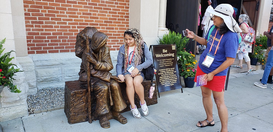 Kimberlie Petrulis takes a photo as her daughter Josephine Petrulis engages with a sculpture called "Be Welcoming" outside St. John the Evangelist Church in Indianapolis July 18, 2024. The two Catholics from the Diocese of Richmond, Va., admired the piece, one of two created by Catholic sculptor Timothy Schmalz for the National Eucharistic Congress. (OSV News photo/Natalie Hoefer, The Criterion)