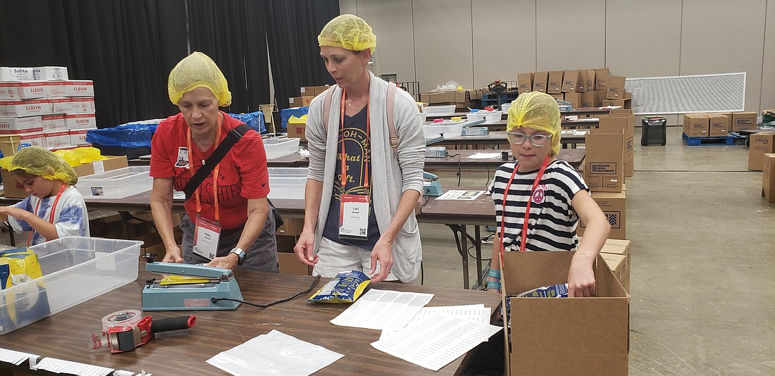 Annabel Cougron, right, places meal packets in a box as her grandmother Patty Arnold, left, and mother Lori Arnold seal the packages July 18, 2024, as part of a service project in the Indiana Convention Center in Indianapolis during the National Eucharistic Congress. (OSV News photo/Natalie Hoefer, The Criterion)