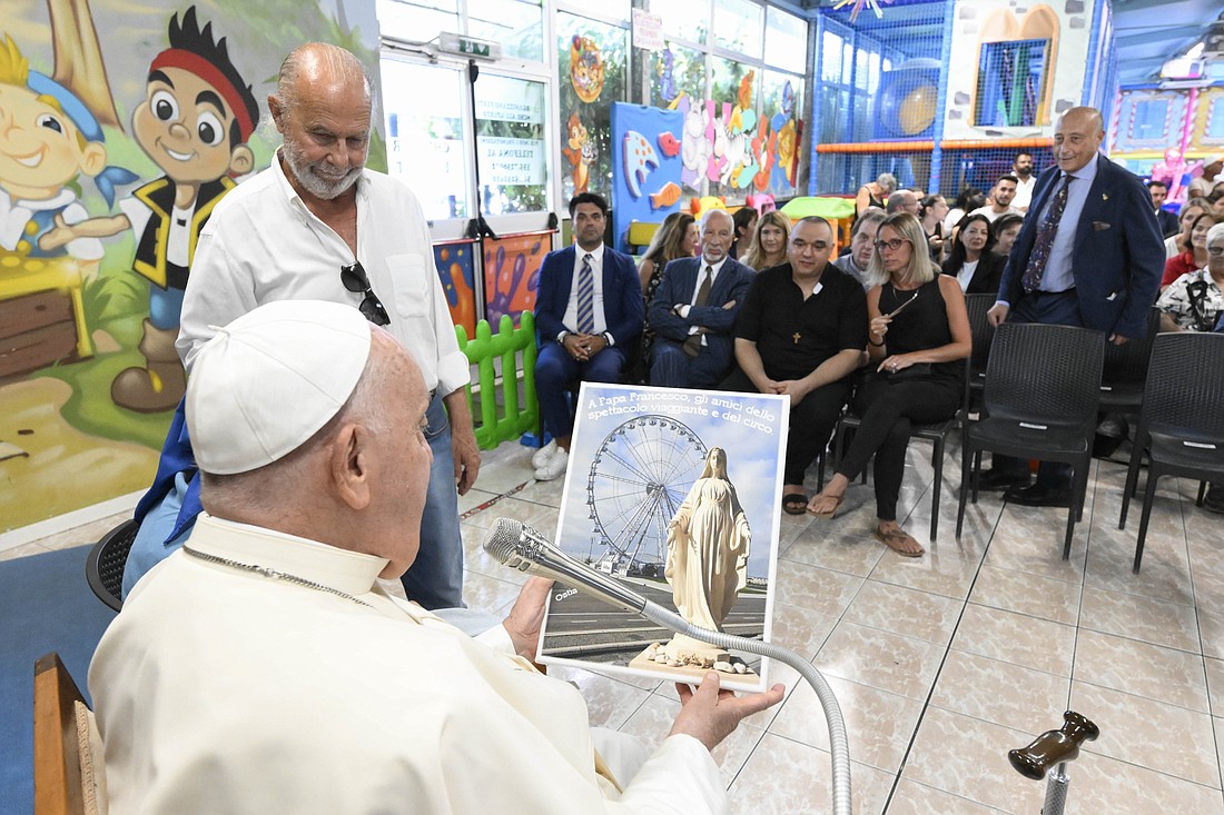 Pope Francis looks at an illustration showing a statue of Our Lady that was recently installed at the "Luna Park di Ostia" amusement park during a visit to the park in Ostia, Italy, July 31, 2024. He visited the park, which is an hour outside of Rome, to greet workers, their families and the two nuns providing pastoral care there. (CNS photo/Vatican Media)