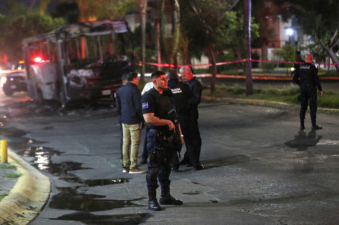 Police officers stand near the burned wreckage of a bus Aug. 9, 2022, that was set on fire by members of the Jalisco New Generation Cartel following the detention of one of its leaders by Mexican federal forces in Zapopan in the Mexican state of Jalisco. (OSV News photo/Fernando Carranza, Reuters)