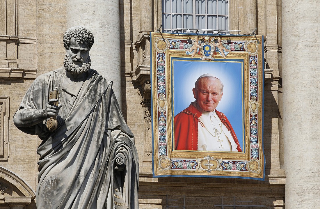 A banner depicting St. John Paul II hangs from the facade of St. Peter's Basilica at the Vatican prior to his canonization in this April 25, 2014, file photo. At left is a statue of St. Peter. With the news that Pope John Paul I will be beatified, some have begun to wonder if being pope is a shortcut to sainthood. (CNS photo/Paul Haring)