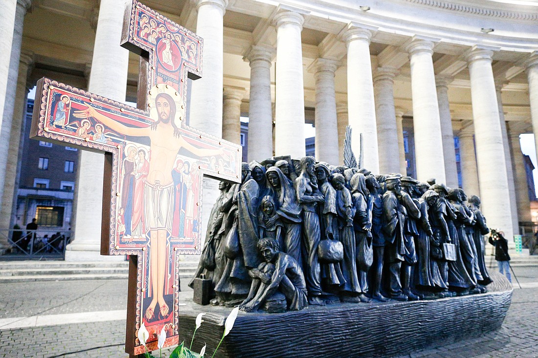 Se observa una cruz frente a "Angels Unawares", una escultura del canadiense Timothy Schmalz, en la Plaza de San Pedro del Vaticano el 19 de octubre de 2023. El Papa Francisco y los miembros de la asamblea del Sínodo de los Obispos se reunieron para rezar por los migrantes y refugiados en torno a la escultura, que representa una barca con 140 figuras de migrantes de diversos periodos históricos y varias naciones. (Foto CNS/Lola Gomez)