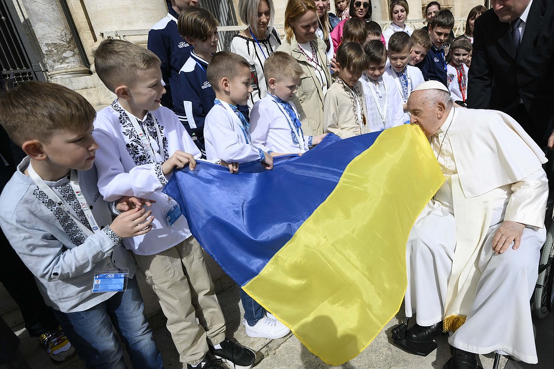 Pope Francis kisses a Ukrainian flag carried by a group of Ukrainian children attending his weekly general audience in St. Peter's Square at the Vatican April 10, 2024. The pope prayed during the audience for peace in Ukraine, in the Holy Land and in Myanmar. (CNS photo/Vatican Media)