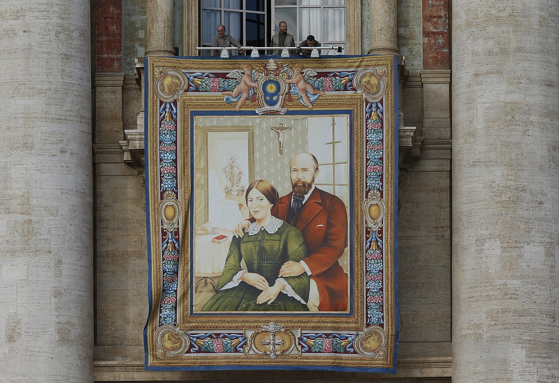 Workers prepare a banner of Louis and Marie Zelie Guerin Martin, the parents of St. Therese of Lisieux, on the facade of St. Peter's Basilica at the Vatican Oct. 16, 2015, in advance of the couple's canonization. (CNS photo/Paul Haring)