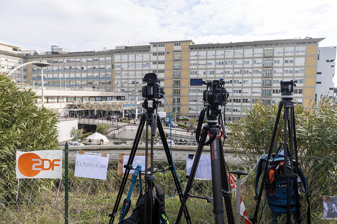 Television cameras are lined up behind homemade signs "reserving" space for various news outlets on a hillside at Rome's Gemelli hospital Feb. 18, 2025. Pope Francis has been an inpatient since Feb. 14. (CNS photo/Pablo Esparza)