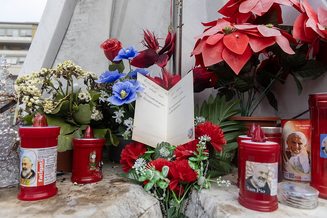 A get-well card for Pope Francis is set among flowers and votive candles at the base of a statue of St. John Paul II outside Rome's Gemelli hospital Feb. 18, 2025. Father Jim Sichko, a priest of the Diocese of Lexington, Ky, told CNS he had left the card for the pope along with a bottle of Kentucky bourbon, which was removed by someone. Father Sichko said he hoped someone took it up to the pope's room. (CNS photo/Pablo Esparza)