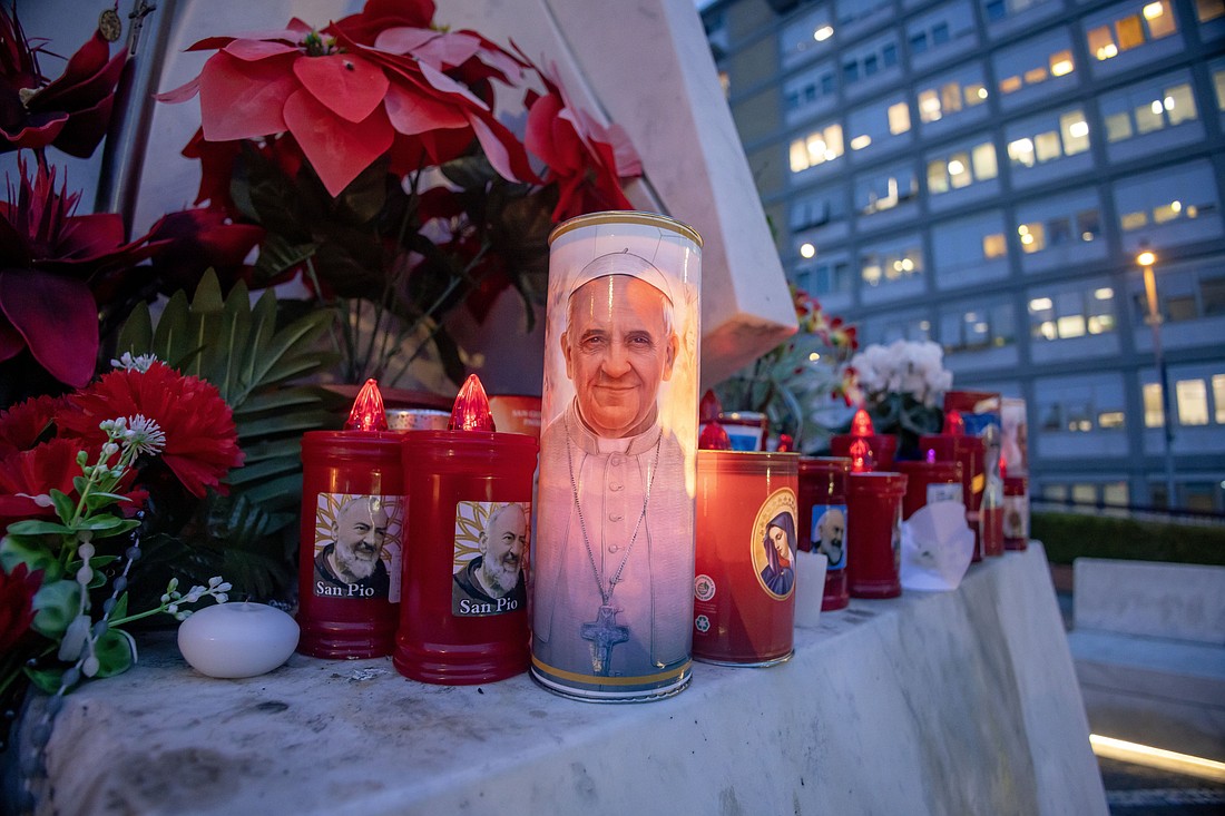 Velas votivas y flores se ven en la base de una estatua de San Juan Pablo II fuera del hospital Gemelli de Roma el 19 de febrero de 2025, donde el Papa Francisco está siendo tratado por una neumonía doble. (Foto CNS/Pablo Esparza)