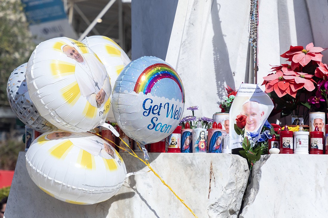 Balloons, votive candles, notes and flowers are seen at the base of a statue of St. John Paul II outside Rome's Gemelli hospital Feb. 23, 2025, where Pope Francis is being treated for double pneumonia. (CNS photo/Pablo Esparza)