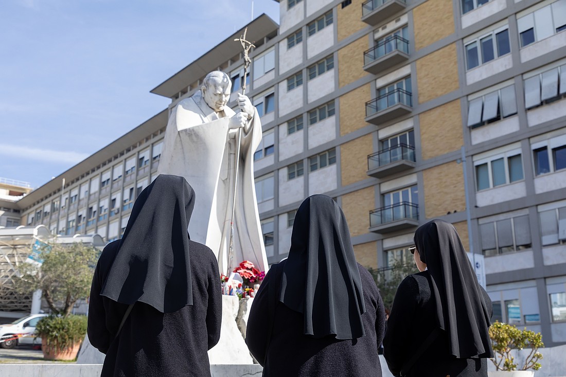 Nuns pray in the courtyard in front of a statue of St. John Paul II outside Rome's Gemelli hospital Feb. 23, 2025, where Pope Francis is being treated for double pneumonia. (CNS photo/Pablo Esparza)