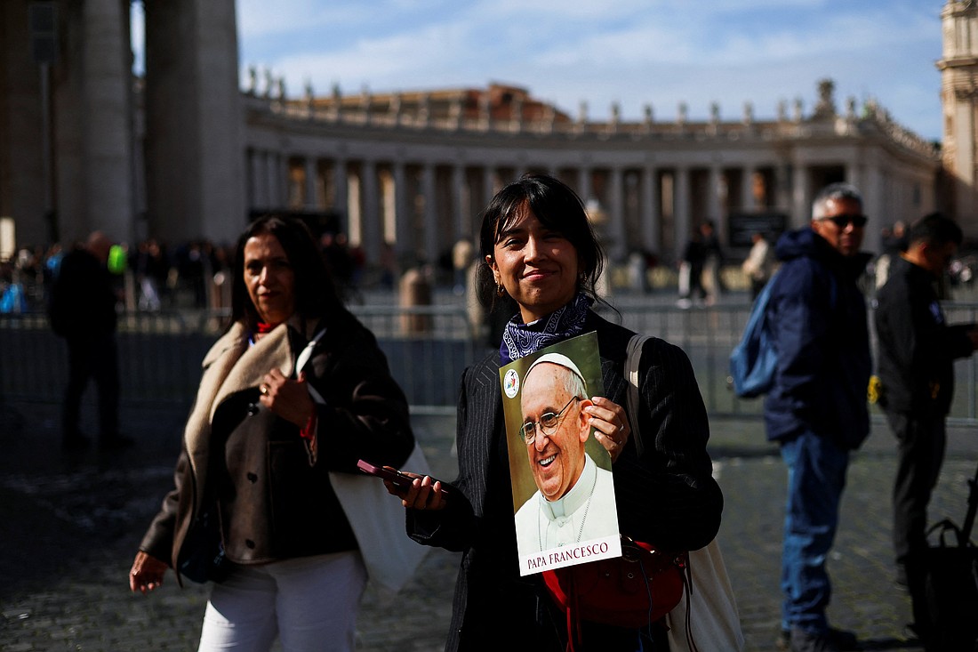 A woman smiles as she holds an image of Pope Francis in St. Peter's Square at the Vatican Feb. 26, 2025, as he continues his treatment for double pneumonia at Rome's Gemelli Hospital. The 88-year-old pontiff had a "restful night" and was sitting upright in an armchair, the Vatican said early Feb. 26. (OSV News photo/Claudia Greco, Reuters).