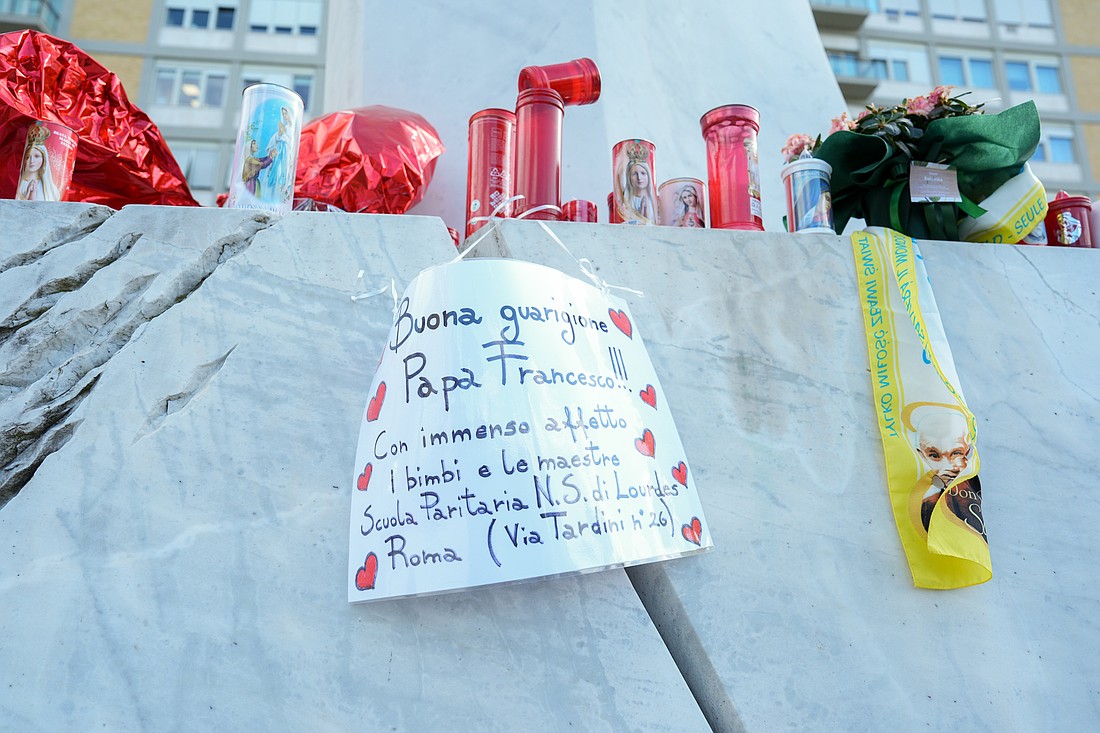 A handwritten sign with prayers for Pope Francis’ recovery is seen among candles and flowers at the base of a statue of St. John Paul II outside Rome’s Gemelli hospital Feb. 27, 2025. The pope has been hospitalized there since Feb. 14. (CNS photo/Lola Gomez)