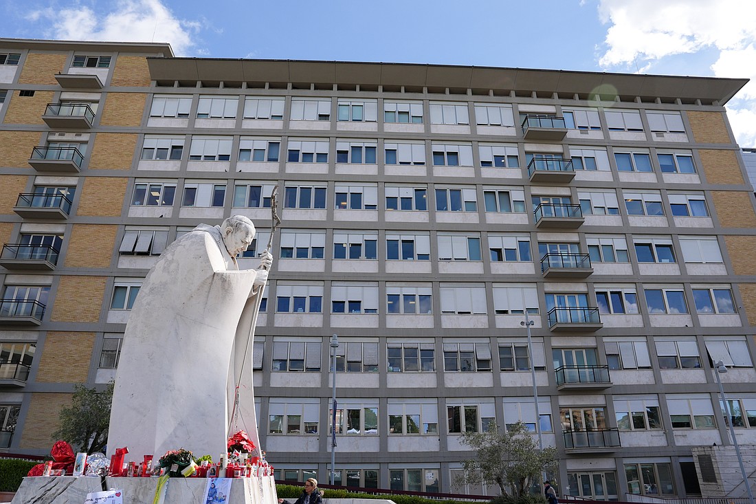 Velas votivas, flores y mensajes para el Papa Francisco se colocan en la base de una estatua de San Juan Pablo II fuera del hospital Gemelli de Roma el 27 de febrero de 2025, mientras el Papa Francisco recibe tratamiento para una doble neumonía. (Foto CNS/Lola Gomez)