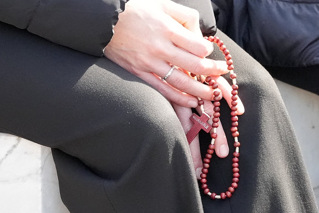 A woman holds a rosary as people pray around a statue of St. John Paul II outside Rome’s Gemelli hospital March 2, 2025. Pope Francis is receiving treatment there for double pneumonia. (CNS photo/Lola Gomez)