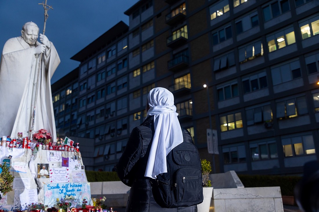 A religious sister prays near a statue of St. John Paul II outside Rome's Gemelli hospital where people have left drawings, votive candles, rosaries, flowers, cards for Pope Francis March 8, 2025. (CNS photo/Pablo Esparza)