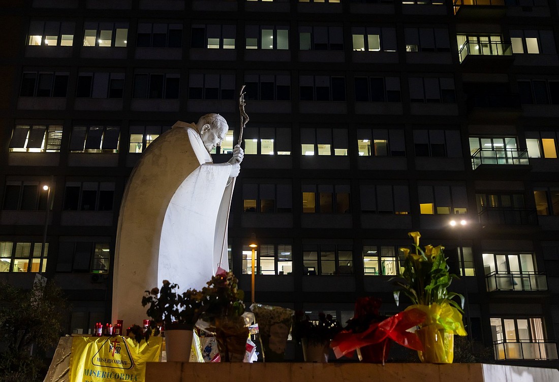 La gente reza cerca de una estatua de San Juan Pablo II en las afueras del hospital Gemelli de Roma, donde la gente ha dejado dibujos, velas votivas, rosarios, flores, tarjetas para el Papa Francisco 8 de marzo 2025. (Foto CNS/Pablo Esparza)