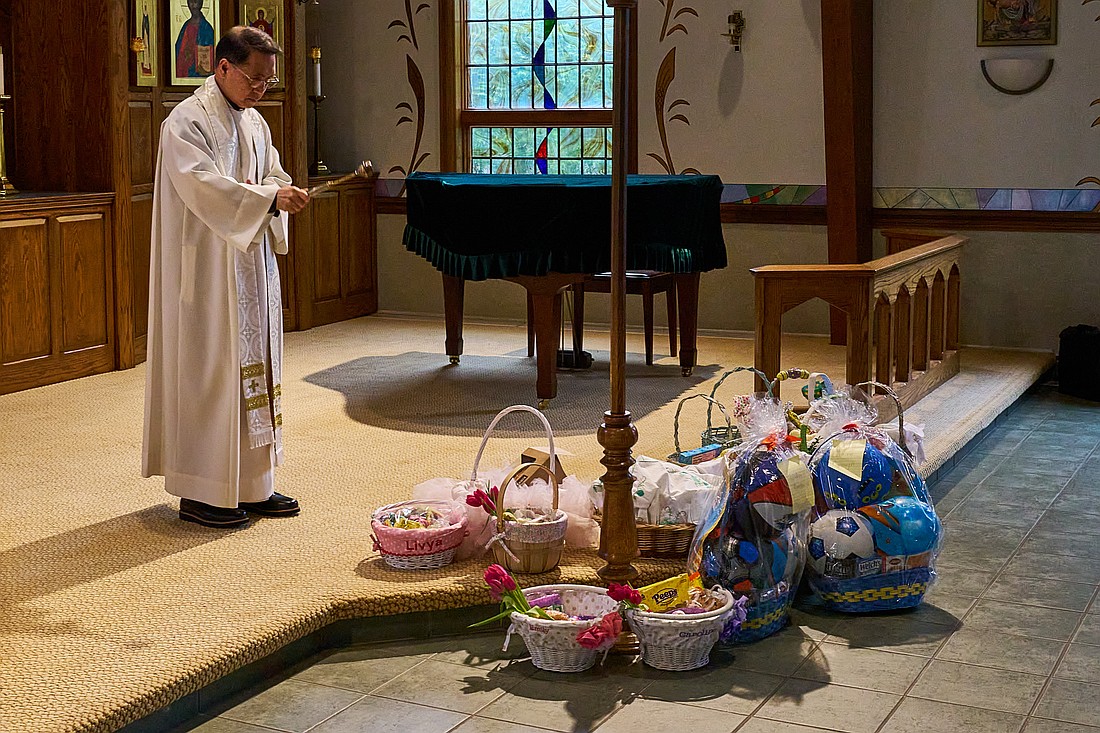Father Angelito Anarcon, pastor of St. Catherine of Siena Parish, Farmingdale, blesses parishioners' baskets filled with Easter foods. Vic Mistretta photo