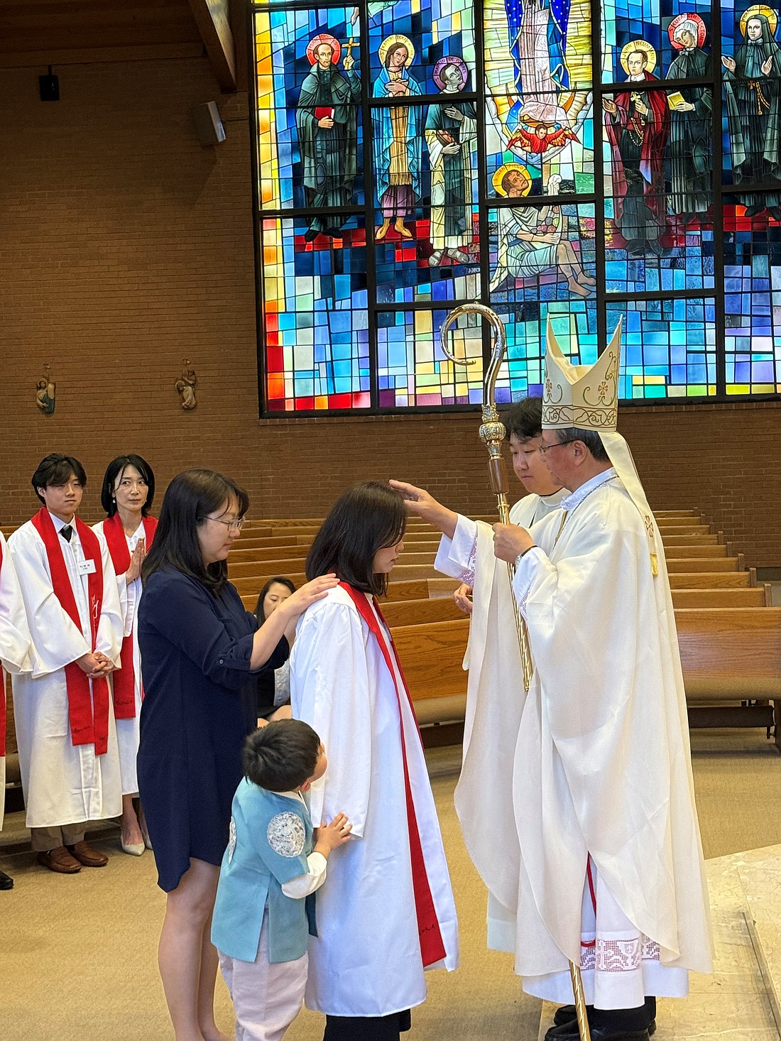 A youngster eagerly looks on as his mom receives the Sacrament of Confirmation from Bishop Kwon. Courtesy photo