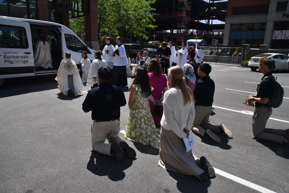 Young adults serving as "perpetual pilgrims" on the National Eucharistic Pilgrimage kneel on May 18, 2025, on the grounds of St. John the Evangelist Church in Indianapolis while the Eucharist is placed in the pilgrimage van. The pilgrimage, which started in Indianapolis, will cross 10 states, 20 dioceses and four Eastern Catholic eparchies before concluding June 22, the feast of Corpus Christi, in Los Angeles. (OSV News photo/Sean Gallagher, The Criterion)