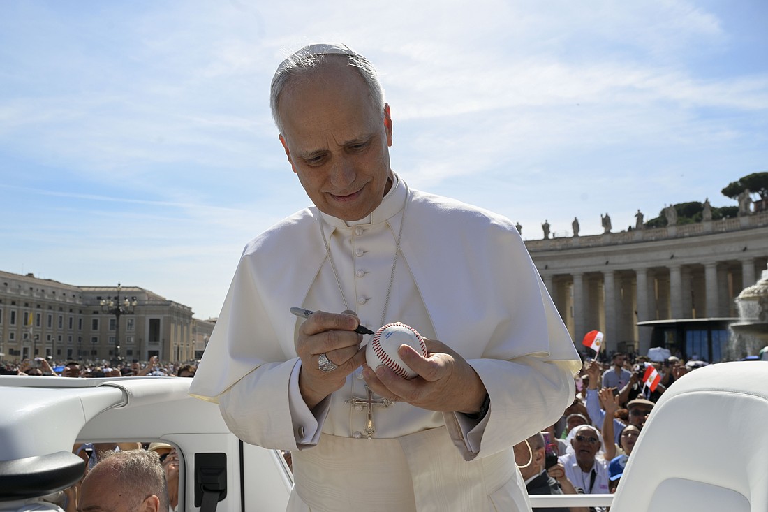 Pope Leo XIV signs a baseball at the Vatican before his weekly general audience June 4, 2025. (CNS photo/Vatican Media)