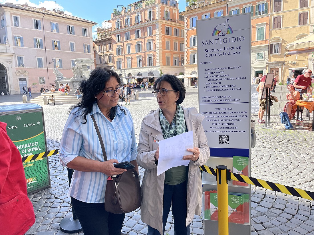 Cecilia Pani, right, talks to a woman about the Community of Sant'Egidio's classes in the Italian language and culture in this file photo taken in Rome's Piazza Santa Maria in Trastevere. (CNS photo/Dale Gavlak)