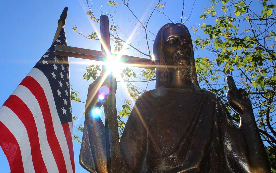 The sun shines through a statue of Christ on a grave marker alongside an American flag at St. Mary Catholic Cemetery in Appleton, Wis., in this 2018 photo. (OSV News file photo/Bradley Birkholz)