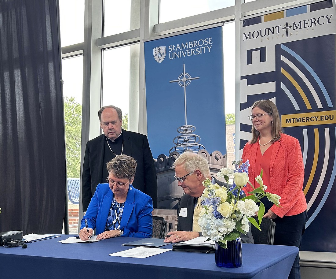 Amy Novak, president of St. Ambrose University in Davenport, Iowa, and Todd Olson, president of Mount Mercy University in Cedar Rapids, sign documents related to completion of the first step of their universities' strategic combination June 27, 2025, at Mount Mercy. Witnessing are Bishop Dennis G. Walsh of Davenport, and Julia Cavallo of the Conference for Mercy Higher Education. (OSV News photo/Barb Arland-Fye, The Catholic Messenger)