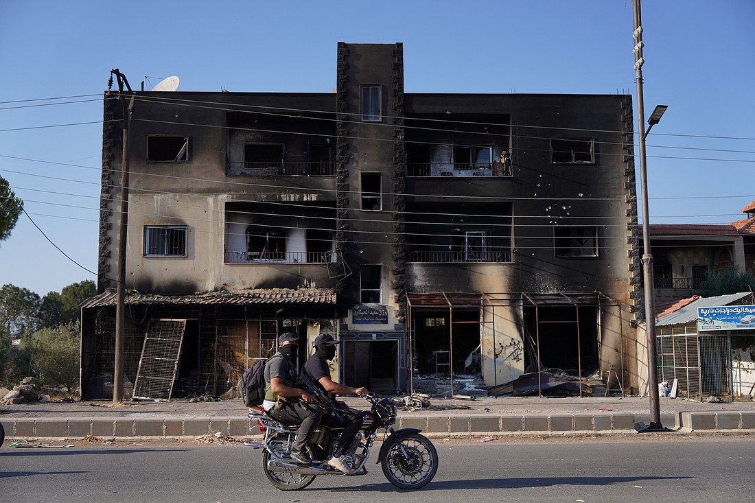 Bedouin fighters ride a motorcycle past a burned building in the village of Al-Mazra'a in Syria's Sweida region July 20, 2025, after days of violence triggered by clashes between Bedouin fighters and Druze factions. (OSV News/Karam al-Masri, Reuters)