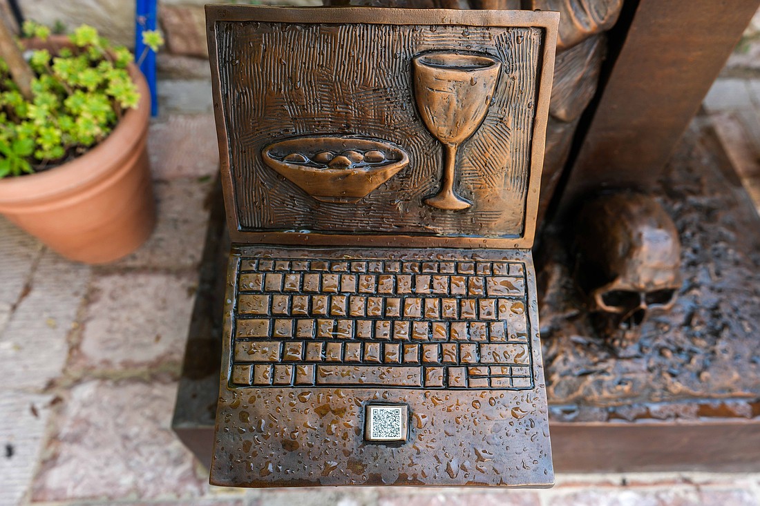 A detail of a sculpture of Blessed Carlo Acutis kneeling at the foot of the crucified Christ is seen in Assisi, Italy, Aug. 21, 2025, after a rainstorm. The bronze work titled "St. Carlo at the Cross" is by Canadian sculptor Timothy Schmalz, and it portrays the young blessed leaning his head against the cross while holding a laptop depicting the sacred vessels for Holy Communion. The QR code brings visitors to the artist's website. (CNS photo/Lola Gomez)