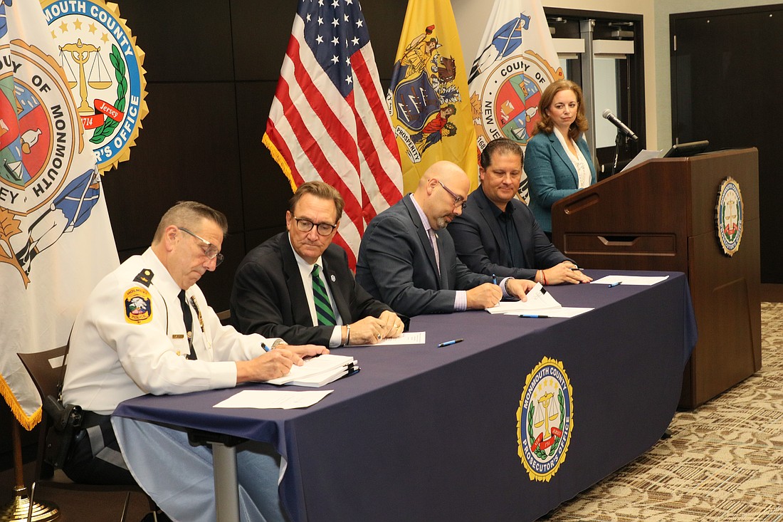 Dr. Vincent de Paul Schmidt, seated second from left, and Monmouth County Prosecutor Raymond S. Santiago, seated second from right, are joined by other law enforcement officials who gathered to witness the signing of the MOA agreement that reflects a strong partnership between school leadership and law enforcement and the commitment to keep students safe. At the podium is Bonnie Milecki, assistant superintendent of development and operations for the Diocese. Staff photo
