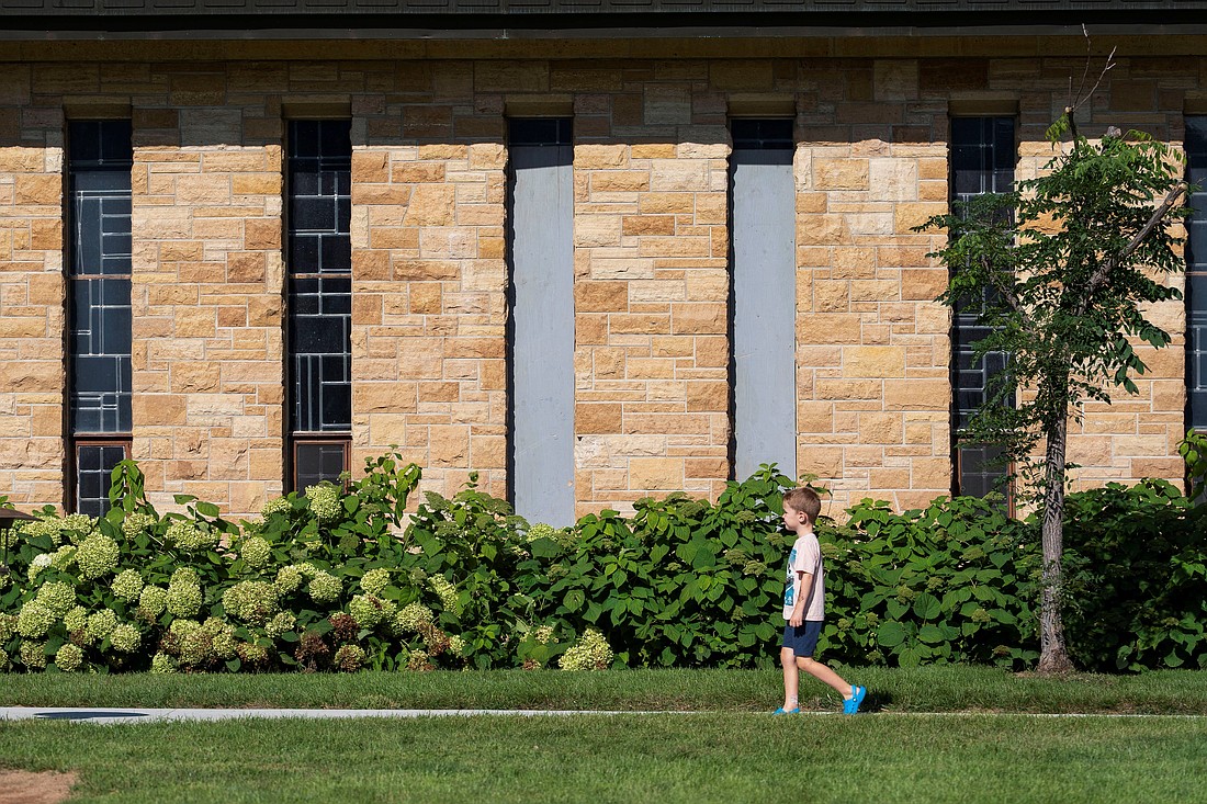 A child walks past boarded up windows outside Annunciation Church in Minneapolis Aug. 28, 2025, which is a home to an elementary school and was the scene of a shooting the day before. A shooter opened fire with a rifle through the windows of the school's church and struck children attending Mass Aug. 27 during the first week of school, killing two and wounding 18 people in an act of violence the police chief called "absolutely incomprehensible." (OSV News photo/Tim Evans, Reuters)