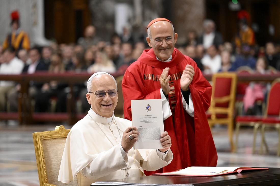 Pope Leo XIV smiles as he holds up his apostolic letter “Drawing New Maps of Hope," marking the 60th anniversary of the Vatican II declaration on Catholic education, which will be celebrated Oct. 28. With Cardinal José Tolentino de Mendonça, prefect of the Dicastery for Culture and Education, looking on, the pope signed the letter before Mass with students from the pontifical universities of Rome in St. Peter's Basilica at the Vatican Oct. 27, 2025. (CNS photo/Vatican Media)