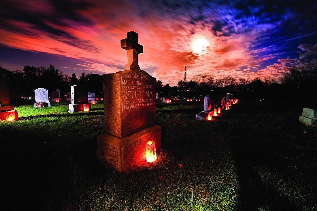 The grave marker of a couple is illuminated with a candle as a full moon shines through clouds in this undated file photo. Catholics pray for the dead during Mass, during designated days such as All Soul's Day, and often ask that Masses be celebrated for our loved ones during the anniversary of their death. (OSV News photo/Lisa Johnston, St. Louis Review)