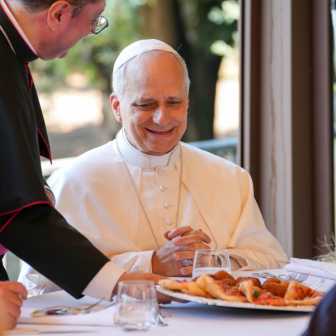 Pope Leo XIV smiles as a tray of food is served during lunch with guests assisted by the Albano diocesan Caritas agency at the Borgo Laudato Si’ in Castel Gandolfo, Italy, Aug. 17, 2025. (CNS photo/Lola Gomez)