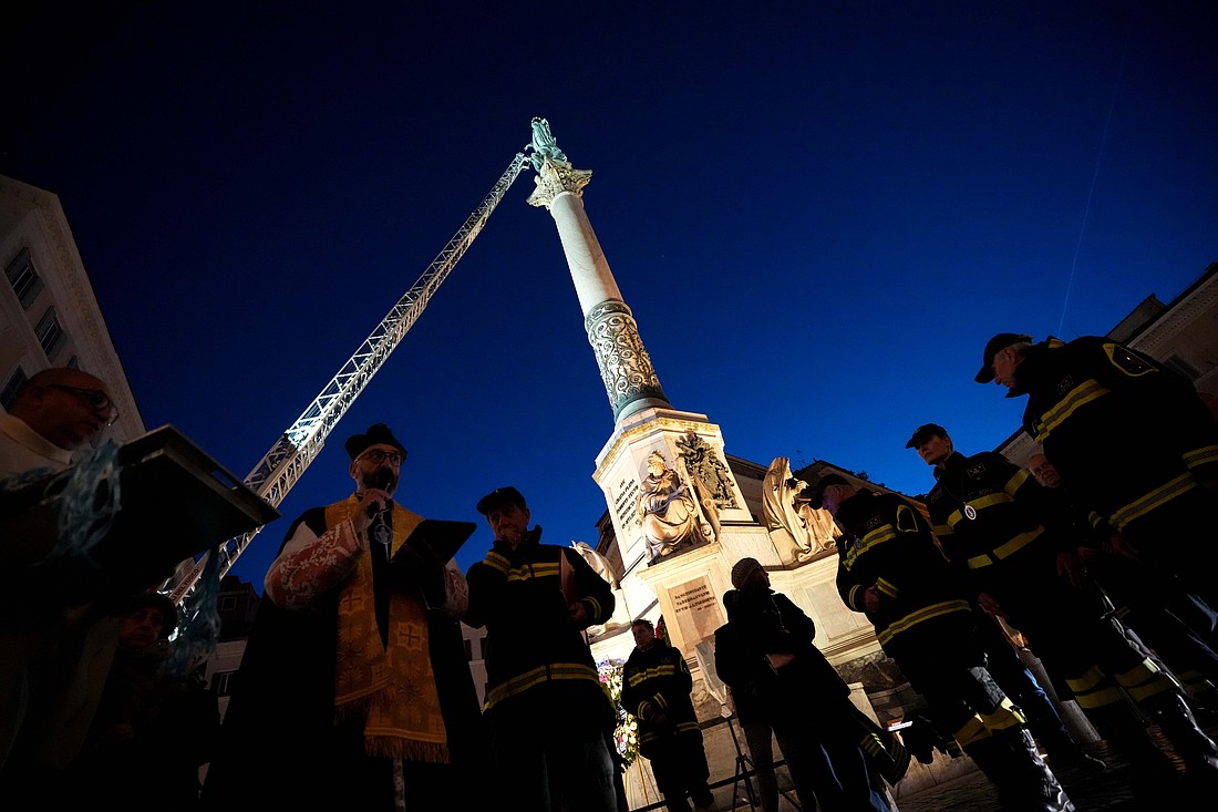 Father Elio Lops, chaplain of Rome's firefighters, blesses firefighters before they place a wreath of flowers on a tall Marian statue overlooking the Spanish Steps in Rome Dec. 8, 2025, the feast of the Immaculate Conception. (CNS photo/Lola Gomez)